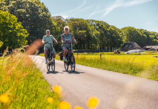 Deux personnes font du vélo sur une route de campagne près d’un hébergement glamping en pleine nature.
