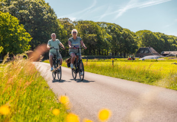 Twee mensen fietsen samen op een landweg bij een glamping-accommodatie, omgeven door natuur.