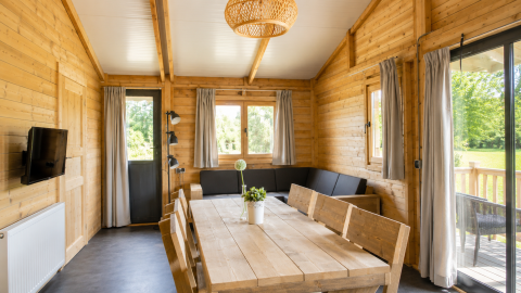 Vista interna di una casa tenda safari in legno al Camping 't Veld, con divano angolare e tavolo da pranzo.
