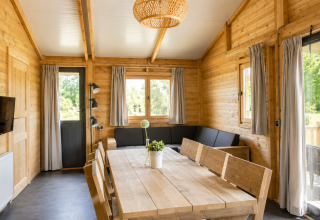 Vista interna di una casa tenda safari in legno al Camping 't Veld, con divano angolare e tavolo da pranzo.