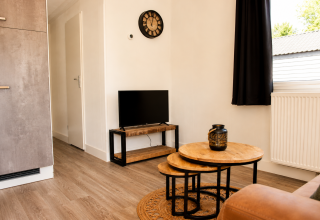 Soggiorno moderno nel Beach chalet al Camping 't Veld, Paesi Bassi con TV, tavolini rotondi e pavimento in legno.