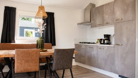 Cocina moderna y comedor en un Beach chalet en Camping 't Veld, Países Bajos, con mesa de madera y armarios grises.