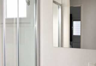 Bagno moderno con doccia in vetro, lavandino bianco e specchio presso il Beach chalet al Camping 't Veld, Olanda.