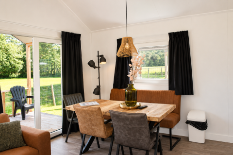 Coin repas dans le Beach chalet au Camping 't Veld, Pays-Bas, avec table en bois et vue sur un champ vert.