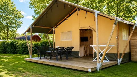 Tienda de safari Comfort con terraza cubierta, muebles de exterior y césped verde rodeado de árboles.