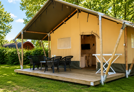 Tenda safari Comfort con veranda in legno coperta, sedie da esterno e prato verde tra gli alberi.
