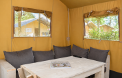 Vista interna della tenda safari Comfort al Camping 't Veld nei Paesi Bassi con tavolo in legno e cuscini.