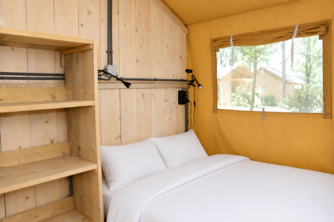 Interior de tienda safari Comfort con estantes de madera y cama en Camping 't Veld, Países Bajos.