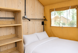 Interno tenda safari Comfort con scaffali in legno e letto al Camping 't Veld nei Paesi Bassi.
