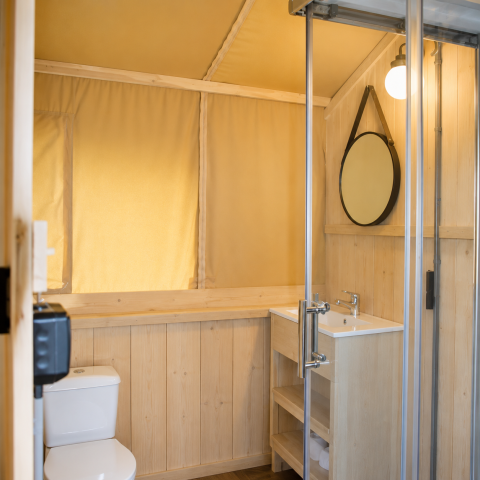 Baño en la tienda safari Comfort de Camping 't Veld en Países Bajos con paneles de madera y ducha moderna.