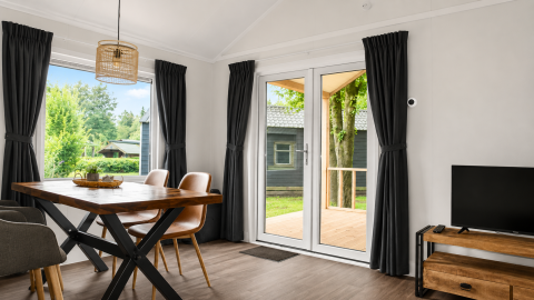 Interno luminoso di chalet con tavolo da pranzo e grandi finestre presso Camping 't Veld, Paesi Bassi.