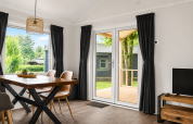 Interno luminoso di chalet con tavolo da pranzo e grandi finestre presso Camping 't Veld, Paesi Bassi.