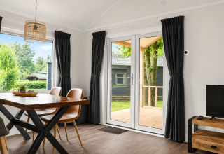 Intérieur lumineux de chalet avec table à manger, grandes fenêtres et terrasse à Camping 't Veld, Pays-Bas.