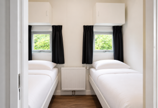 Camera con due letti singoli, biancheria bianca e tende nere presso Beach house, Camping 't Veld.