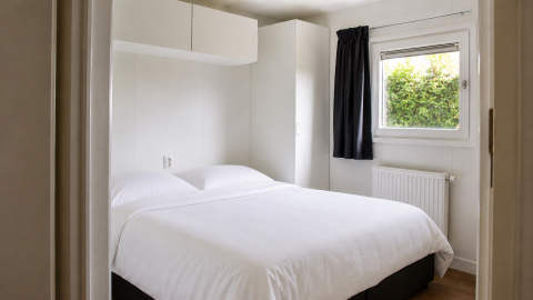 Bedroom inside Beach house with hottub at Camping 't Veld, Netherlands, with double bed, window, and cabinet.