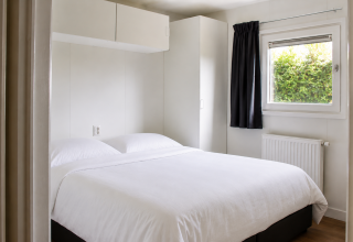 Bedroom inside Beach house with hottub at Camping 't Veld, Netherlands, with double bed, window, and cabinet.