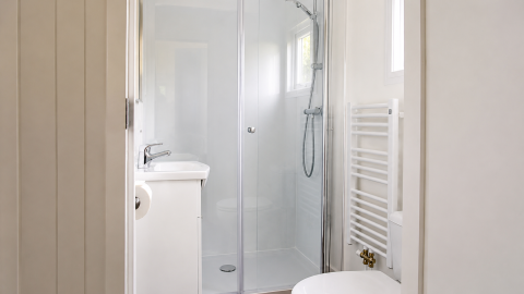 Salle de bain lumineuse avec douche, lavabo et sèche-serviettes au Beach house chalet au Camping 't Veld.
