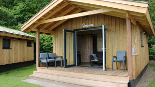 Acogedora casa pequeña de madera con terraza y sillas en Camping de Koeksebelt, Países Bajos.