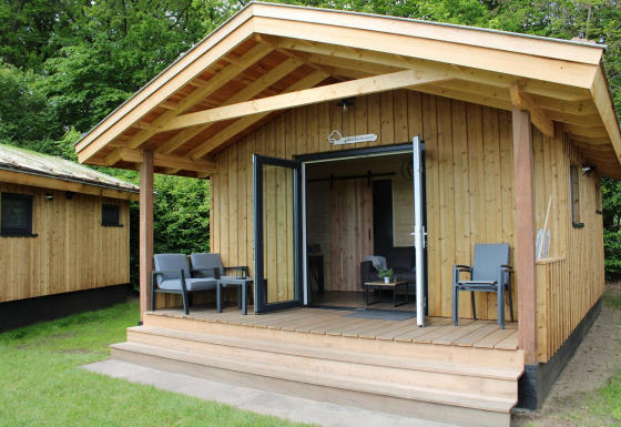 Acogedora casa pequeña de madera con terraza y sillas en Camping de Koeksebelt, Países Bajos.