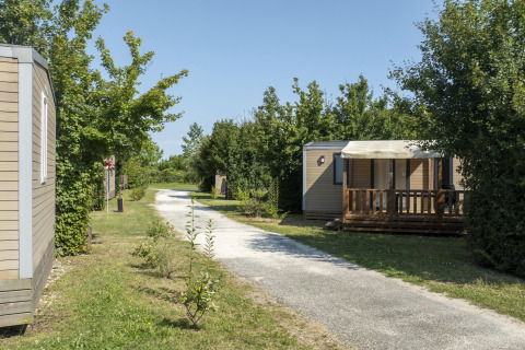 Mobil-homes près d’un chemin de gravier au Seasonova Camping Le Plan d’Eau, Nouvelle-Aquitaine, France.