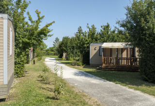 Mobile homes by a gravel path surrounded by trees at Seasonova Camping Le Plan d’Eau, Nouvelle-Aquitaine, France.