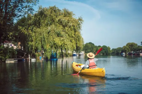 Person paddling a yellow kayak on a calm river near Saint Yrieix sur Charente, surrounded by green trees.