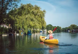Person paddling a yellow kayak on a calm river near Saint Yrieix sur Charente, surrounded by green trees.
