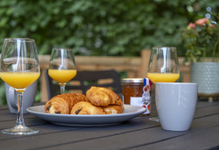 Petit-déjeuner en plein air avec croissants, jus d’orange, café et confiture à Seasonova Camping Le Plan d’Eau.