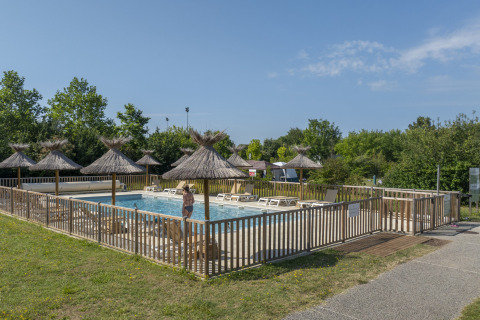 Swimming pool with loungers and straw umbrellas at Seasonova Camping Le Plan d’Eau, Nouvelle-Aquitaine, France.