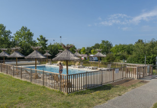 Swimming pool with loungers and straw umbrellas at Seasonova Camping Le Plan d’Eau, Nouvelle-Aquitaine, France.