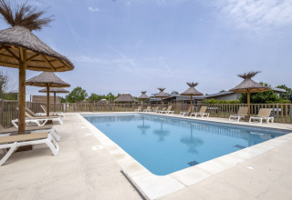 Outdoor swimming pool with sun loungers and straw umbrellas at Seasonova Camping Le Plan d’Eau, Nouvelle-Aquitaine.