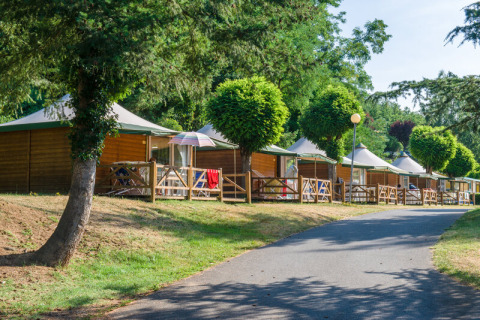 Række af hyggelige hytter og telte omgivet af grønne træer på Seasonova Camping Le Val de Coise i Frankrig.