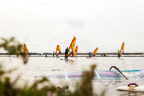 Windsurfistas disfrutan en el parque vacacional Lauwersmeer en Groningen, Países Bajos, bajo un cielo nublado.