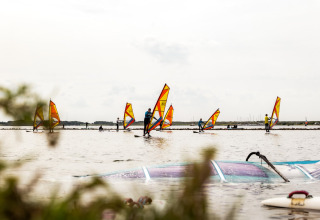 Windsurfer si godono l’acqua nel parco vacanze Lauwersmeer a Groningen, Paesi Bassi, in una giornata nuvolosa.
