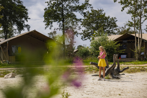 Niña con camiseta rosa y falda amarilla en el parque de vacaciones Lauwersmeer, Groningen, con tiendas al fondo.