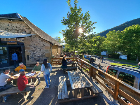 Persone sedute all'aperto ai tavoli in legno al Seasonova Camping Les Rives d'Olt et Aubrac, Occitania, Francia.