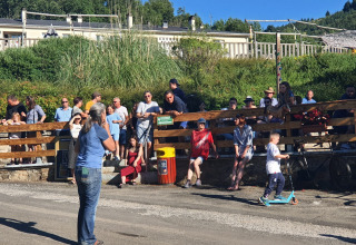 Des gens profitent d’une journée ensoleillée dans un camping; un garçon roule en trottinette.