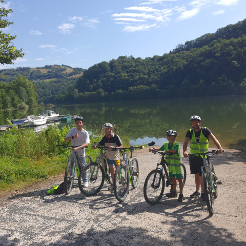 Quatre personnes avec des vélos et des casques près d'un lac à Seasonova Camping Les Rives d'Olt et Aubrac en Occitanie, France.