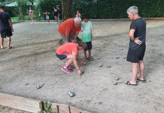 Des personnes jouent à la pétanque sur un terrain sablonneux au camping Seasonova Les Rives d'Olt et Aubrac, Occitanie.