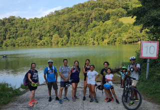 Un gruppo di persone con biciclette e zaini vicino a un lago al Seasonova Camping Les Rives d'Olt et Aubrac in Occitania, Francia.