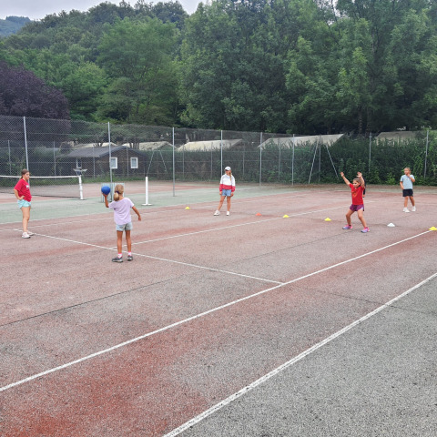 Children play a ball game on a tennis court at Seasonova Camping Les Rives d'Olt et Aubrac in Occitanie, France.