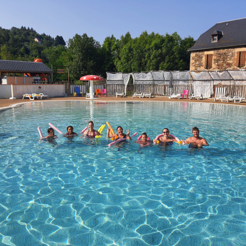 Famiglie e amici si godono una giornata di sole in piscina al Seasonova Camping Les Rives d'Olt et Aubrac in Occitania, Francia.