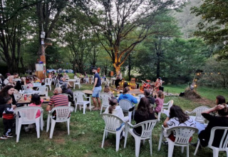 Concert en plein air dans un camping d’Occitanie, France, avec public installé sur des chaises blanches en plastique.