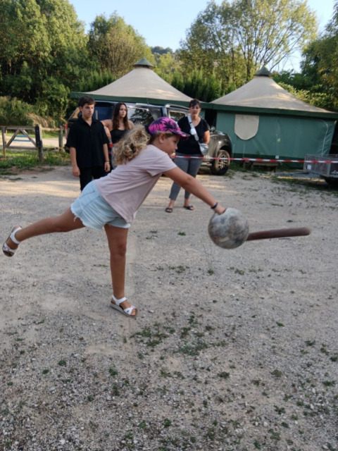 Une fille avec un bandeau rose joue à un jeu de balle en plein air au Seasonova Camping Les Rives d'Olt et Aubrac.
