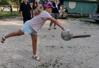 Une fille avec un bandeau rose joue à un jeu de balle en plein air au Seasonova Camping Les Rives d'Olt et Aubrac.