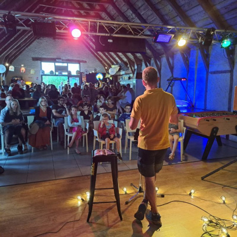 Man on stage entertaining audience at Seasonova Camping Les Rives d'Olt et Aubrac in Occitanie, France.