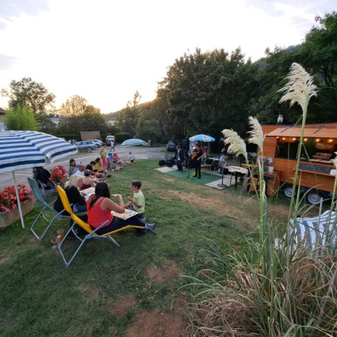 Scena all'aperto al Seasonova Camping Les Rives d'Olt et Aubrac in Occitania, Francia, con persone che mangiano e musica dal vivo.