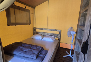 Interior de tienda safari en Slow Lodge, Camping Seasonova Lac de Bournazel, Francia, con cama y ventilador.