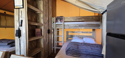 Vista interna della tenda safari 'Slow Lodge' con letto a castello, matrimoniale e scaffali a Camping Seasonova.