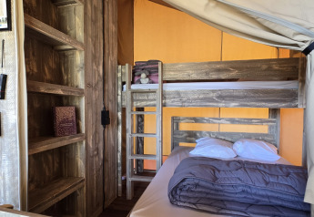Interieur van de 'Slow Lodge' safaritent met stapelbed, tweepersoonsbed en houten rek bij Camping Seasonova.